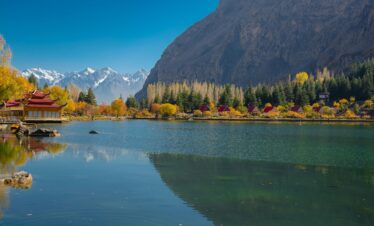 Peaceful autumn scene of a lake and mountains in Skardu, with vibrant foliage and a clear sky.